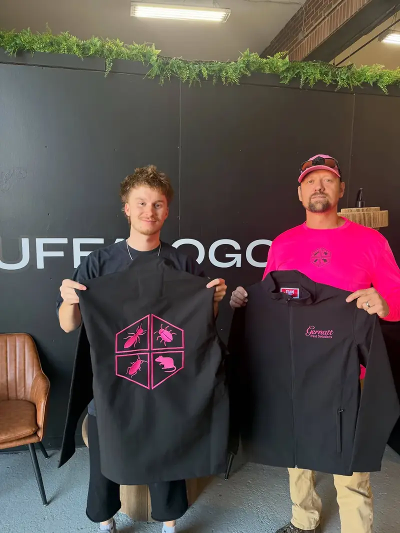 Two people holding new pink Gernatt Pest Solutions shirts in the branded shop
