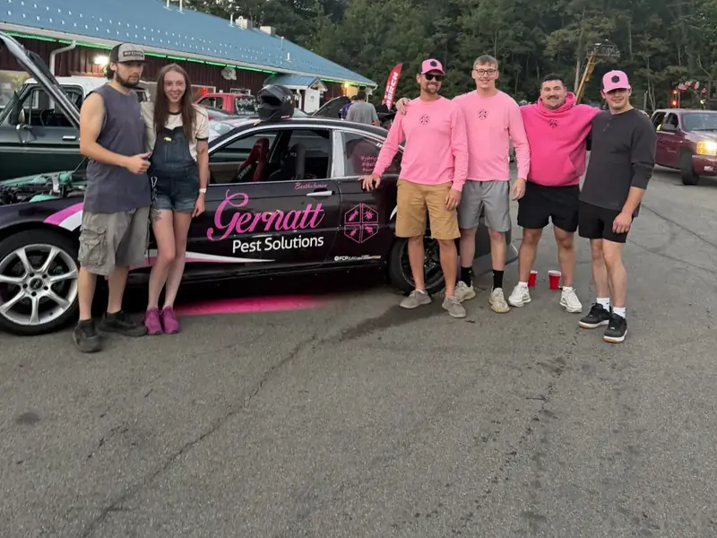 Gernatt Pest Solutions crew in pink shirts beside the wrapped company car at an event