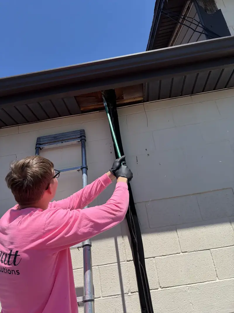 Gernatt technician in a pink shirt on a ladder treating the roofline of a block building