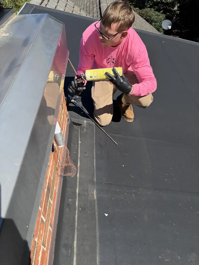 Technician in pink sealing chimney flashing on a roof to keep out bats and wildlife