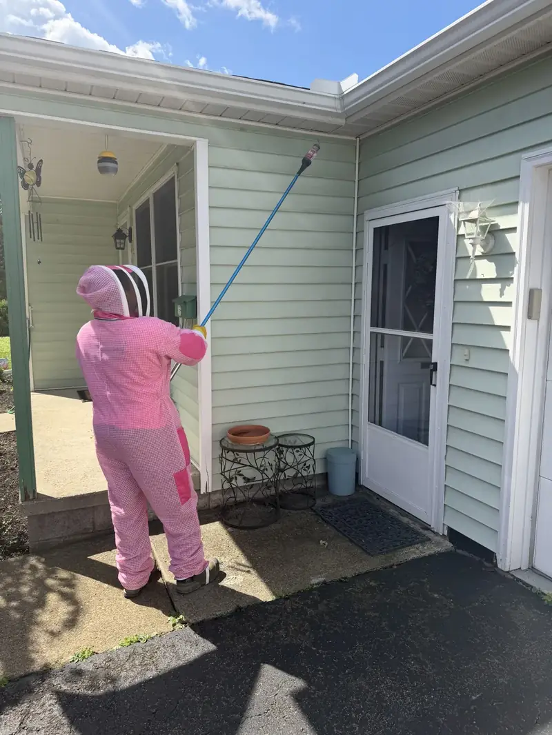 Gernatt technician in a pink protective suit treating a home's eaves with an extension pole