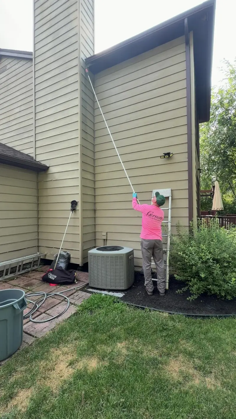 Technician in a pink shirt treating tall siding with an extension pole